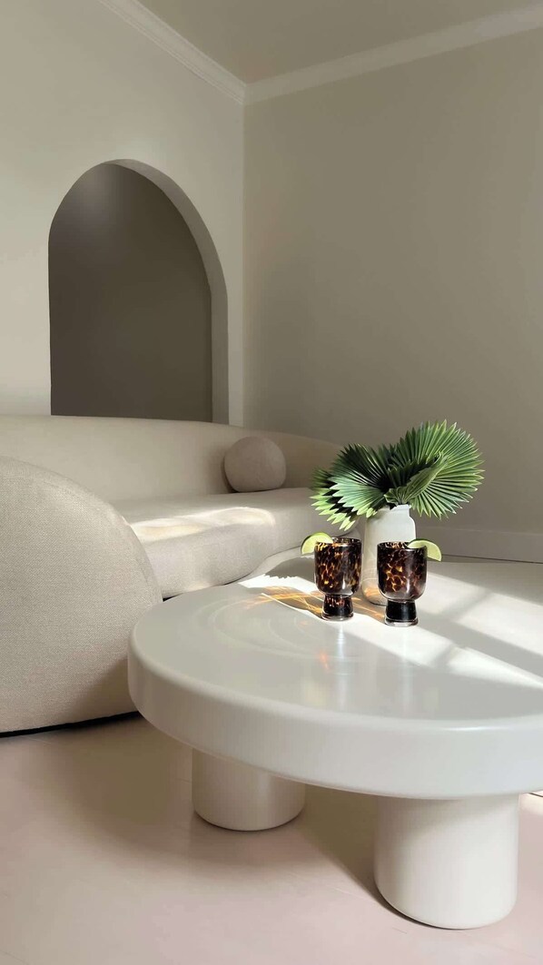 Un salon moderne avec une table basse ronde blanche, un canapé et une plante en pot.