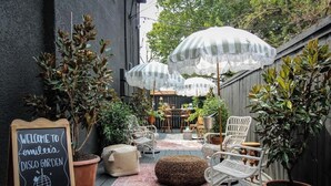 A cozy outdoor patio with wicker chairs, striped umbrellas, and a chalkboard sign welcoming to Emilee's Disco Garden. - Mr. Nomad: Casa Bohem in Uptown (Dallas)
