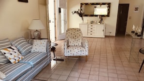 Una sala de estar con un sofá a rayas, un sillón estampado y una mesita. Hay un mueble con cajones y un espejo encima.