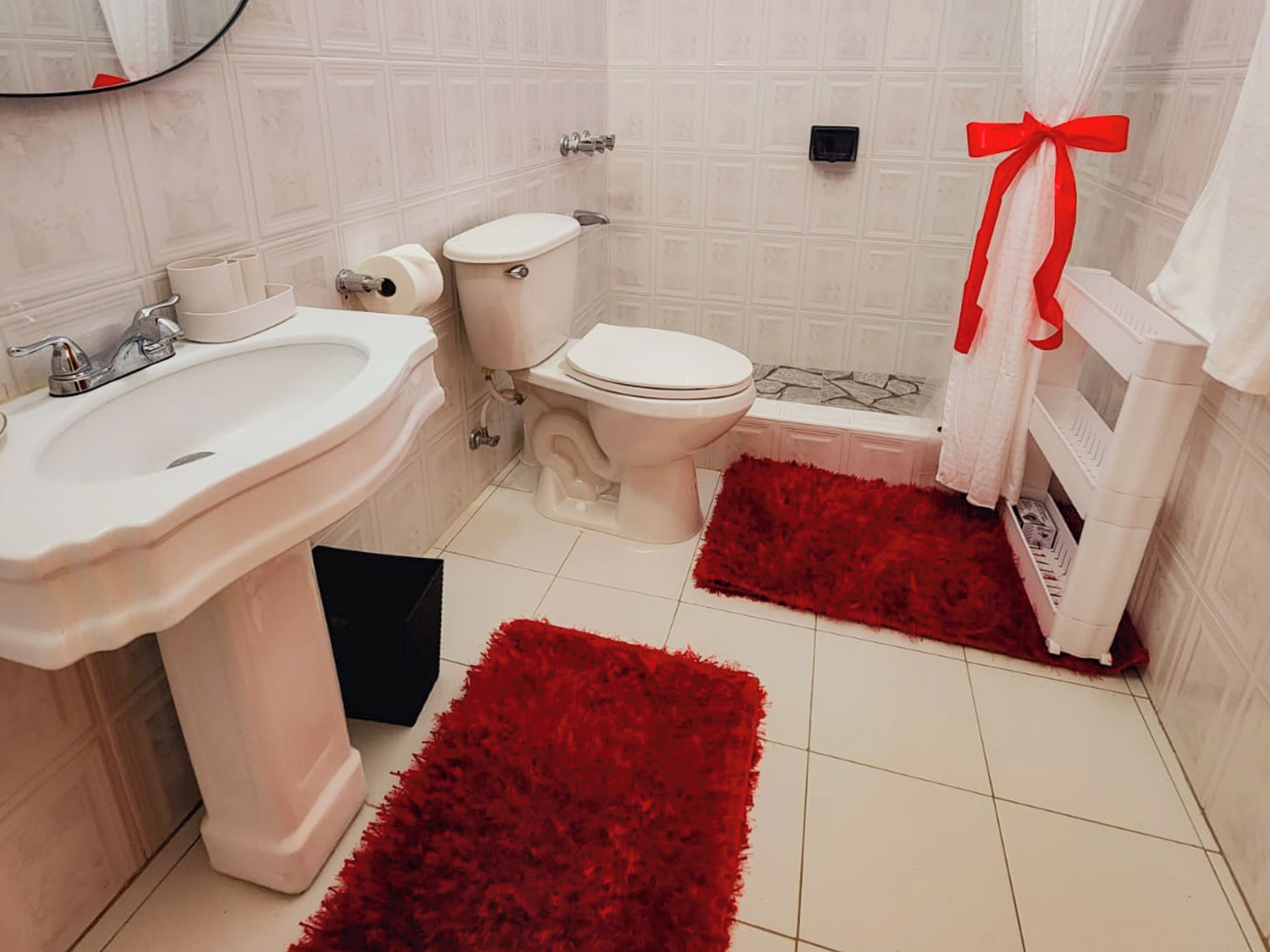 A bathroom with a white sink, toilet, and bathtub. There are two red rugs on the floor.