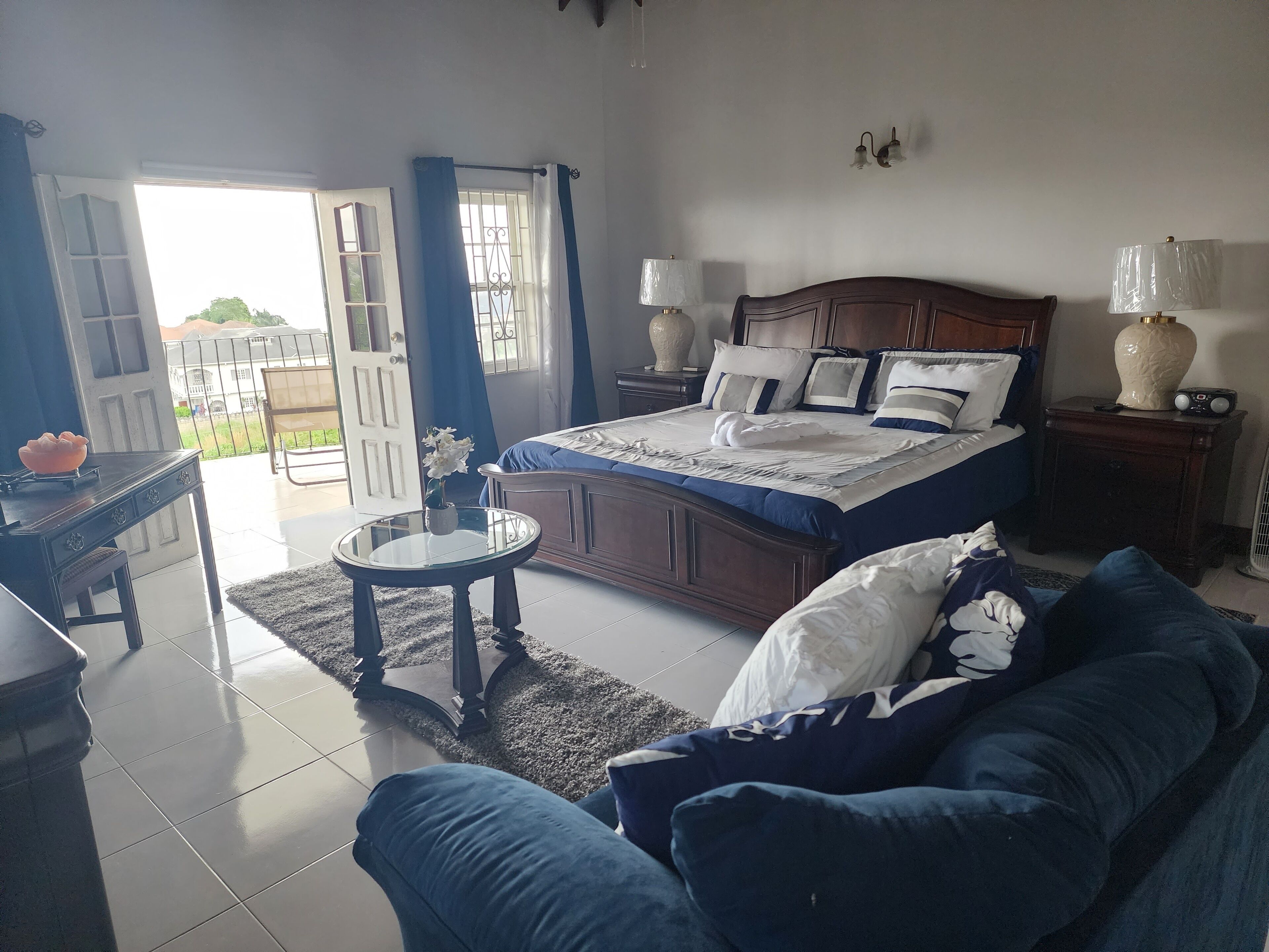 A bedroom with a bed, bedside tables, a sofa, a small round table, and a view of the outside.