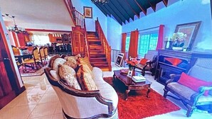 Amplia sala de estar con una imponente escalera, una chimenea y un comedor al fondo.