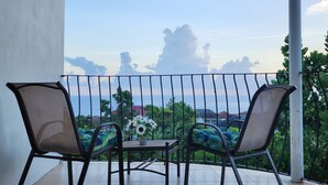 Un balcón con dos sillas y una mesita, con vistas panorámicas al mar y edificios a lo lejos.