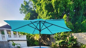 Zona junto a la piscina con una mesa y sillas de vidrio, una sombrilla turquesa y una piscina.