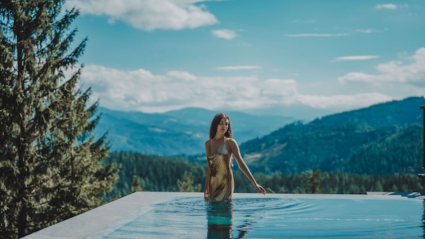 A woman standing in a swimming pool with a mountainous landscape in the background.