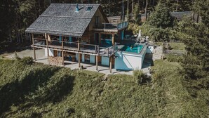 A wooden cabin with a balcony and a swimming pool, surrounded by dense forest.