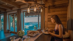 A wooden interior with a dining area, a view through large windows, and a rustic chandelier.