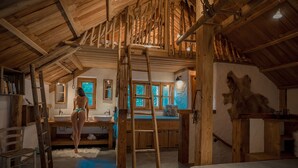 A rustic wooden interior with a loft bedroom, a bathroom with a large window, and a ladder leading to the loft.