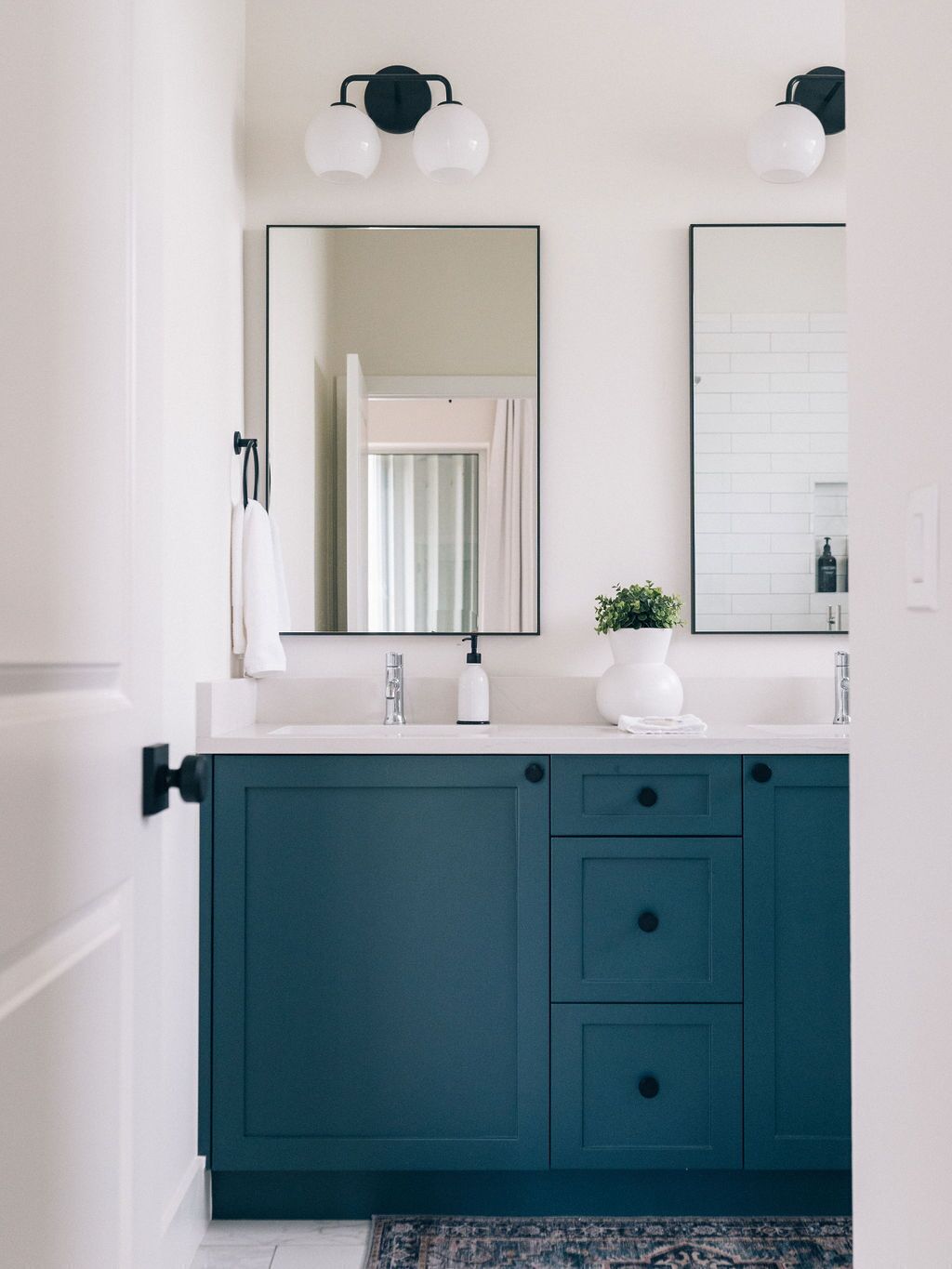 Un baño con un lavamanos blanco, armarios color turquesa, dos luces empotradas en la pared y un espejo.