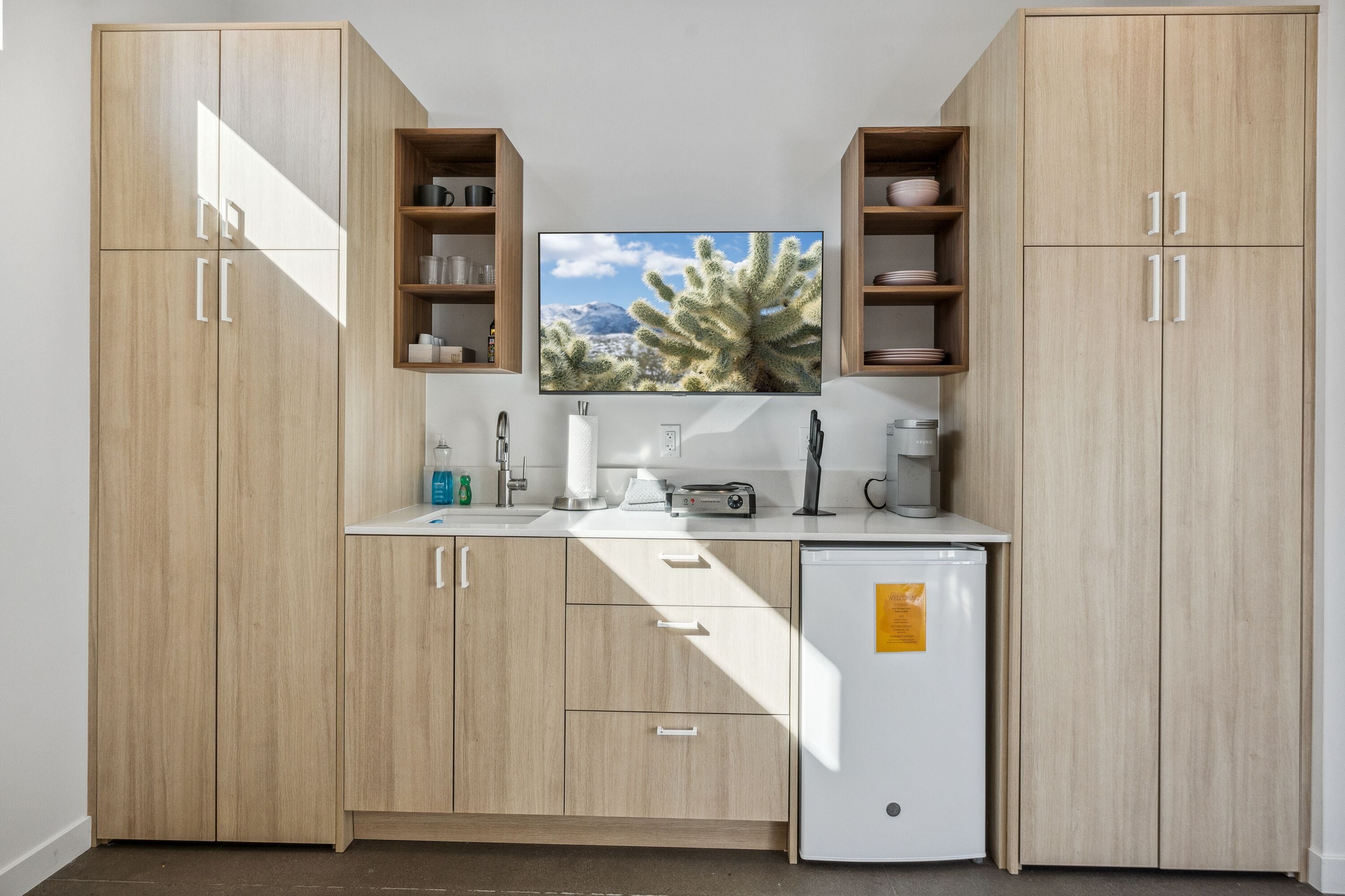 A compact kitchen with wooden cabinets, a refrigerator, and a countertop with various appliances and storage.