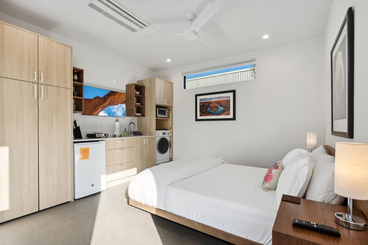 Una habitación de hotel moderna con cama, escritorio, lavadora y kitchenette.