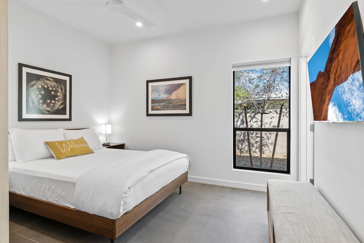 Un dormitorio moderno con una cama, un banco y dos cuadros enmarcados en la pared.