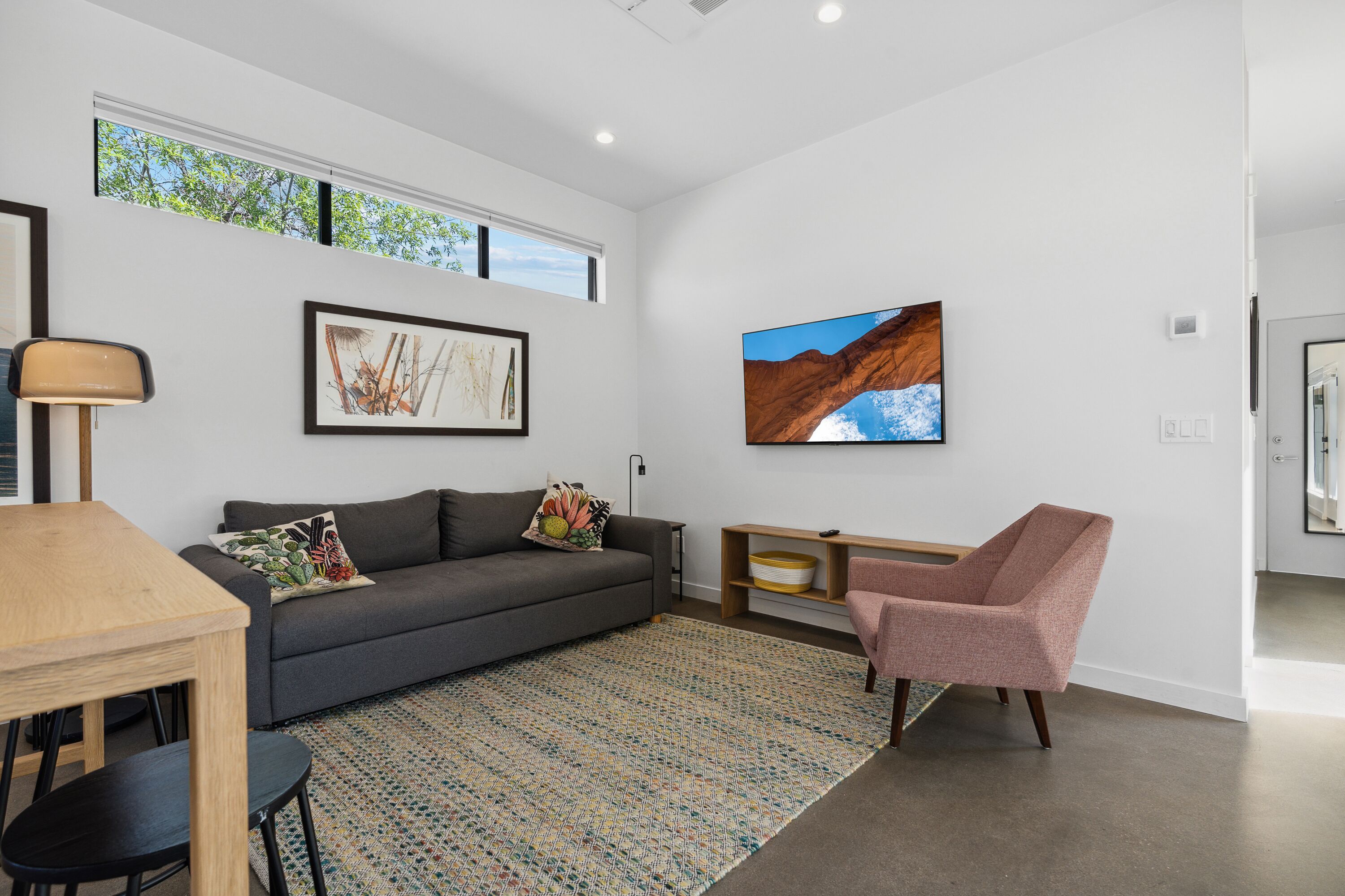 A modern living room with a grey sofa, a wooden coffee table, a pink armchair, and a large painting on the wall.