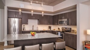 A modern kitchen with dark wood cabinets, stainless steel appliances, and a central island with bar stools. - 2BD/Austin - Full Kitchen, W/D, Balcony, Fire Pit! (Austin)