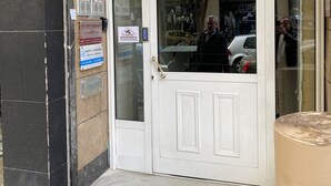 Entrada de edificio con una puerta blanca, un escalón y un letrero en la pared.