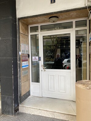A building entrance with a white door, a small step leading up, and a sign on the wall.