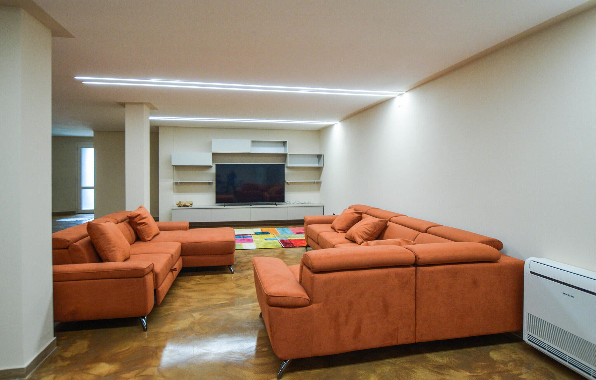 Un soggiorno moderno con un divano componibile, una TV a schermo piatto ed scaffalature integrate.