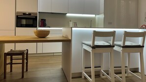 Una cocina moderna con armarios blancos, una mesa de comedor de madera y dos taburetes blancos.