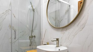 A bathroom with a glass-enclosed shower, a round mirror, and a wooden countertop with a sink. - Escape 2 Nazaré - Private garage in the city (Nazaré)