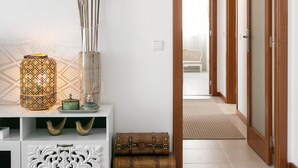 A hallway with a white console table, a green vase with pampas grass, a patterned lantern, and a wooden chest. - Escape 2 Nazaré - Private garage in the city (Nazaré)