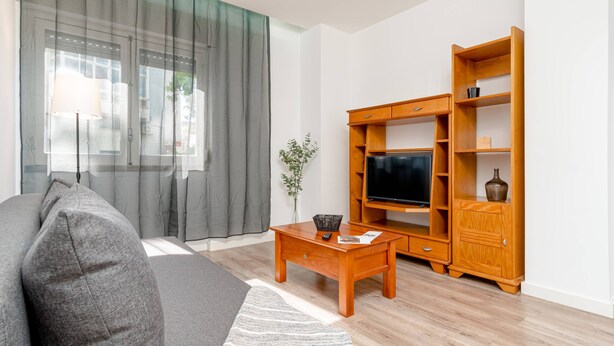 A living room with a sofa, TV stand, wooden cabinet, and a small table. - Cozy Retreat in the Southbank of Lisbon (Almada)