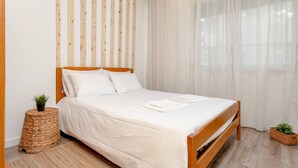 A neatly made bed with white linens, a wooden headboard, and a woven side table with a plant. - Cozy Retreat in the Southbank of Lisbon (Almada)