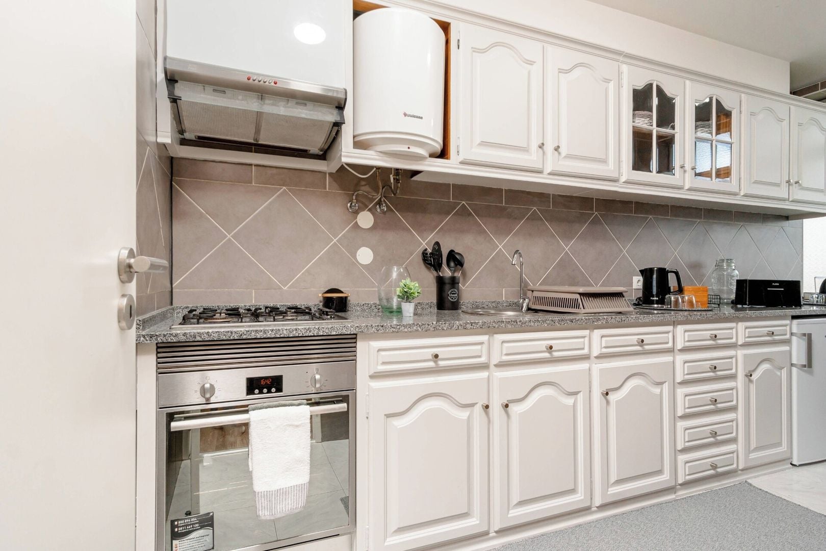 A modern kitchen with white cabinetry, a built-in oven, and a stainless steel range hood.