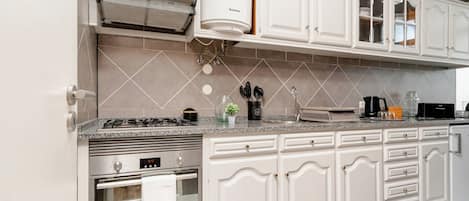 A modern kitchen with white cabinetry, a built-in oven, and a stainless steel range hood.