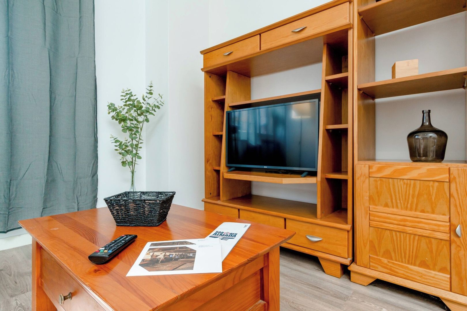 Ein Holz-Fernsehschrank mit einem Flachbildfernseher, einer Fernbedienung und einer Pflanze auf einer Kommode.