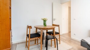 A small, neatly arranged room with a wooden cabinet, a round wooden table with two chairs, a vase with flowers, and a door leading to another room. - Cozy Retreat in the Southbank of Lisbon (Almada)