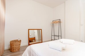 Une chambre à coucher avec un lit, un miroir, une étagère en bois et un panier en osier.