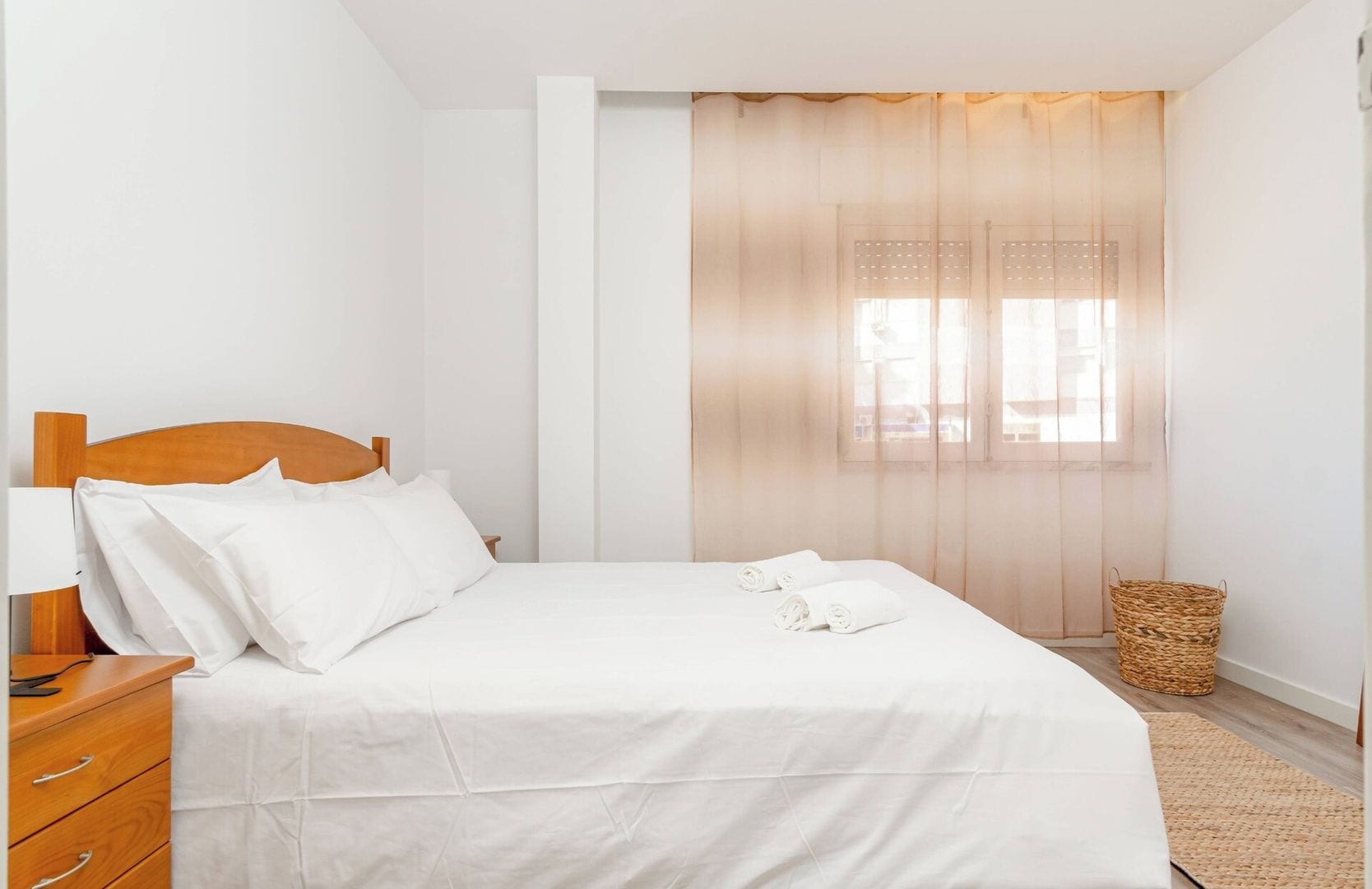 Una cama bien hecha con sábanas blancas, un cabecero de madera y una mesita de noche con lámpara.
