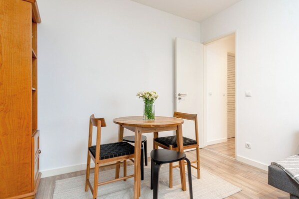 A small room with a round wooden table, two chairs, a vase with flowers, and a wardrobe.