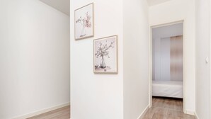 A room with a wooden floor, white walls, and a door leading to a bedroom. There are two framed pictures on the wall. - Cozy Retreat in the Southbank of Lisbon (Almada)
