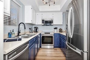 A modern kitchen with white cabinets, a stainless steel refrigerator, a microwave, and an oven.