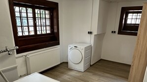 A laundry room with two washing machines, a radiator, and a window with a view.