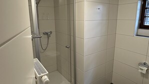 A small bathroom with a shower, toilet, and a window.