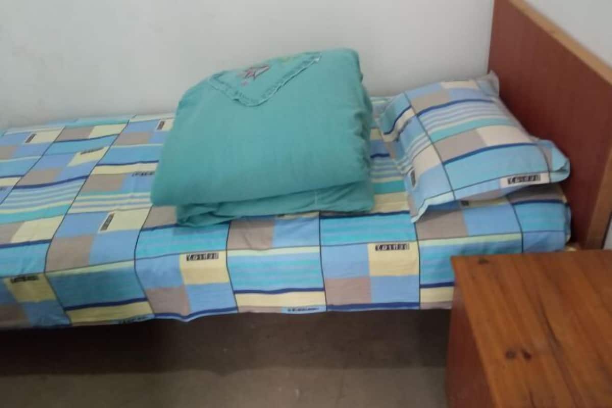 A single bed with a checkered bedspread, a teal pillow, and a wooden nightstand.