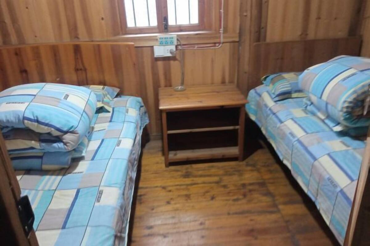A small, wooden room with two beds, a small table, and a window.