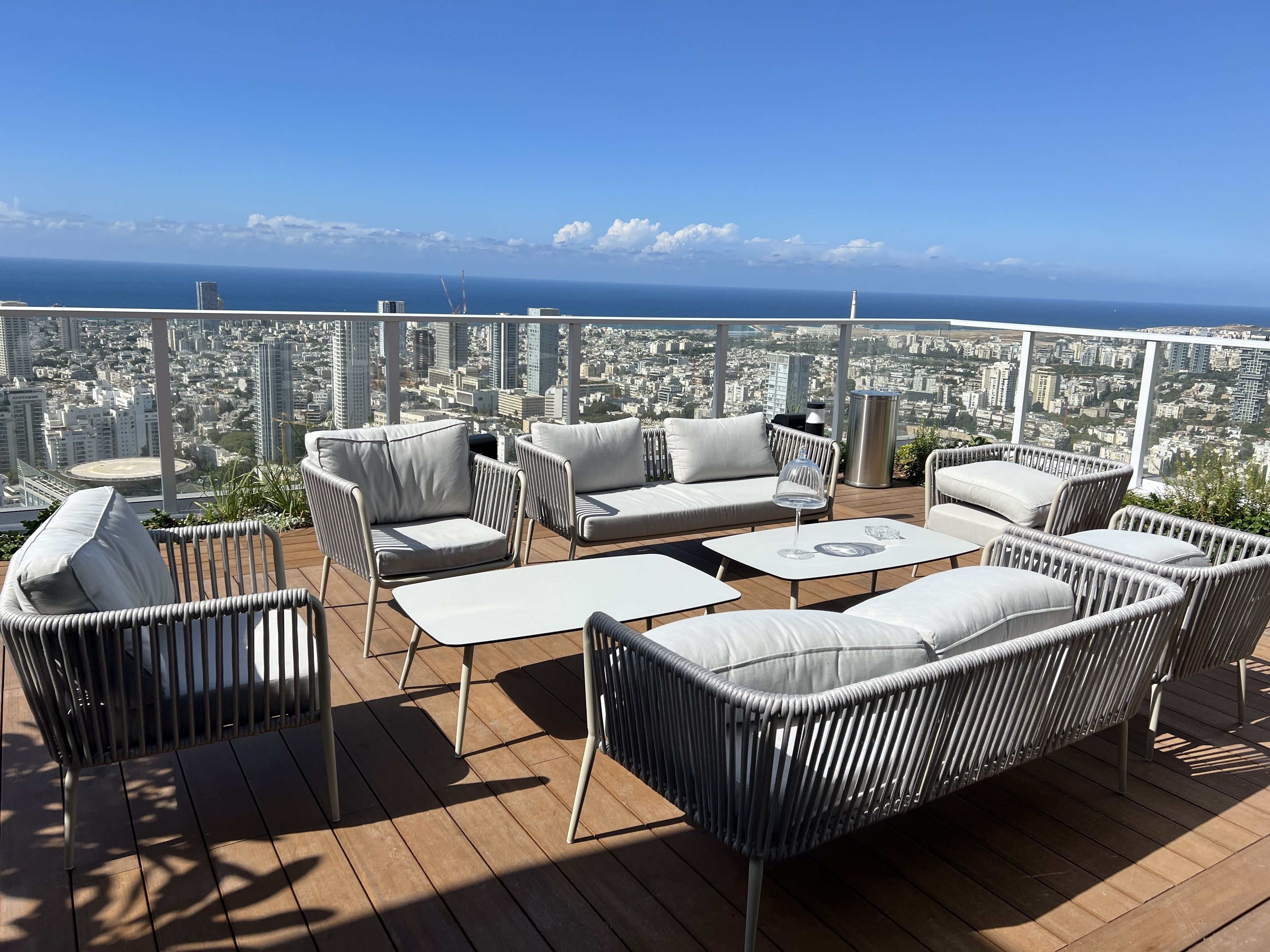 Eine Dachterrasse mit Korbmöbeln, Blick auf eine Stadtlandschaft und einen klaren Himmel.