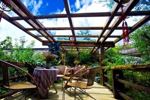 A covered outdoor seating area with wicker chairs and a table, surrounded by lush greenery. - Gudao Gudao Renjia Inn (Lijiang)