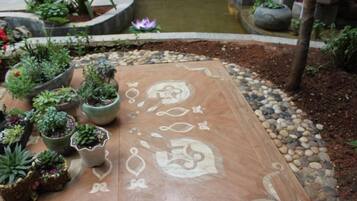 Un jardín con un sendero decorado, plantas en macetas y un pequeño elemento de agua.