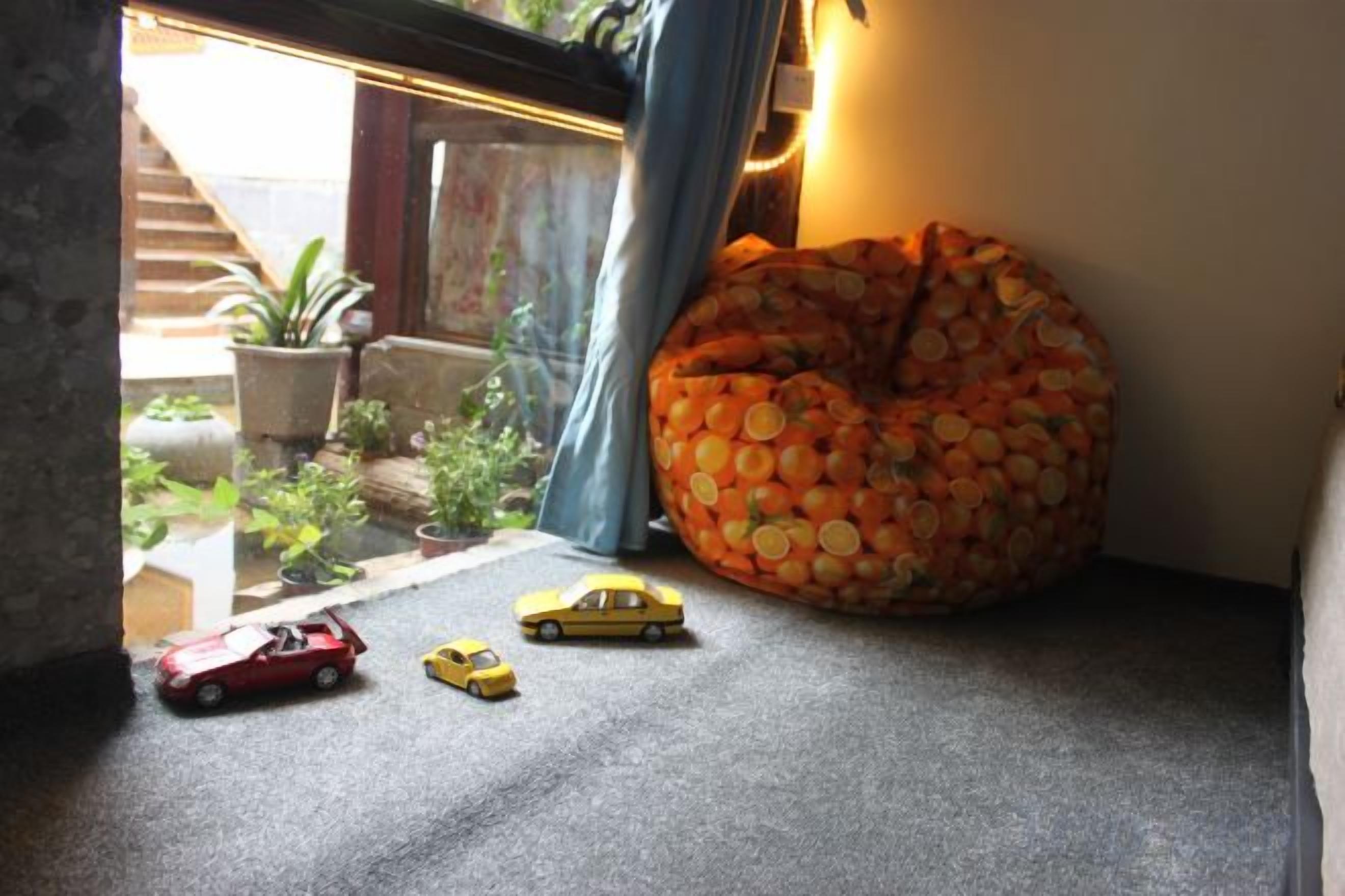 Una habitación con un sillón de peluche, un coche de juguete pequeño y una ventana que da a plantas.