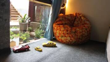 Una habitación con un sillón de peluche, un coche de juguete pequeño y una ventana que da a plantas.