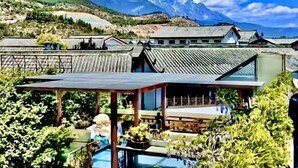 A traditional Japanese-style building with a modern extension, surrounded by lush greenery and mountains in the background. - Gudao Gudao Renjia Inn (Lijiang)