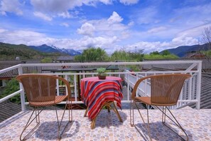 A balcony with two wicker chairs and a table, overlooking a mountainous landscape. - Gudao Gudao Renjia Inn (Lijiang)