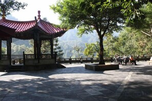 A pavilion with a traditional roof, surrounded by stone flooring, and a view of a mountainous landscape. - Gudao Gudao Renjia Inn (Lijiang)