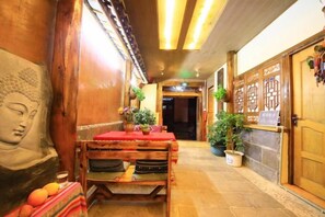 A corridor with a Buddha statue, a wooden table with a red cloth, and a reception area with a wooden door and plants. - Gudao Gudao Renjia Inn (Lijiang)