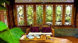 A traditional wooden room with a tatami mat table, a woven sofa, and a view through a lattice window. - Gudao Gudao Renjia Inn (Lijiang)
