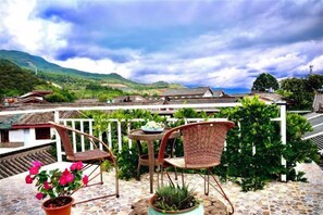 A terrace with wicker chairs and a table, overlooking a village with traditional houses and a mountainous landscape. - Gudao Gudao Renjia Inn (Lijiang)